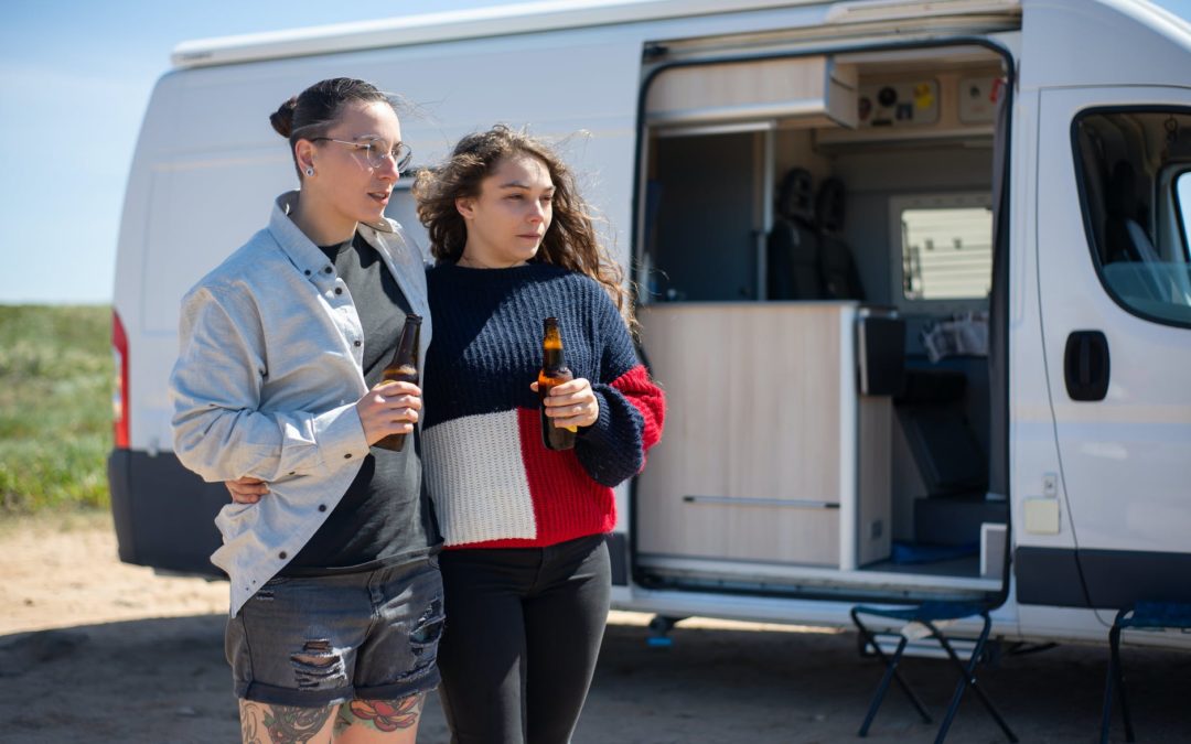 women holding beer bottles while standing beside a motorhome